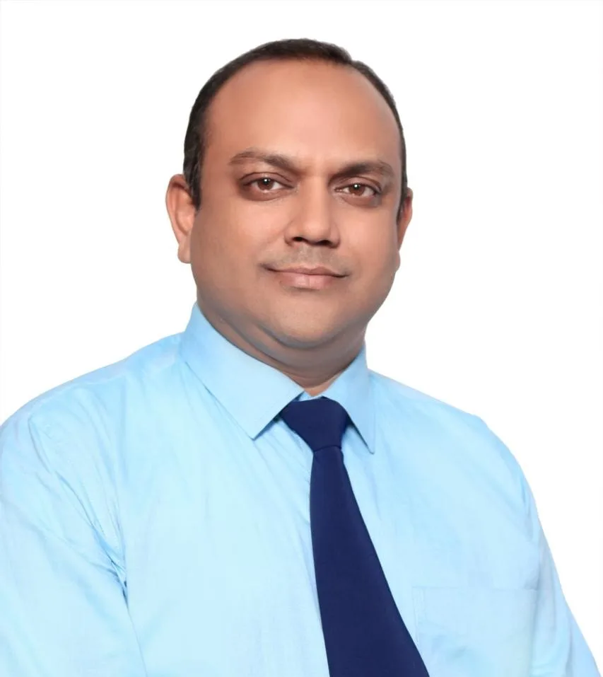 Portrait of a man in a light blue shirt and navy tie, smiling confidently with a neutral background.